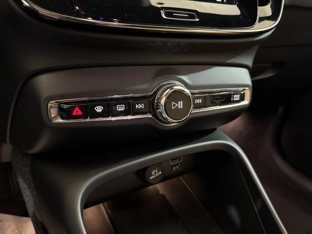 Gros plan sur la console centrale noire du Volvo XC40 Recharge T5 avec commandes multimédia et bouton hazard rouge.