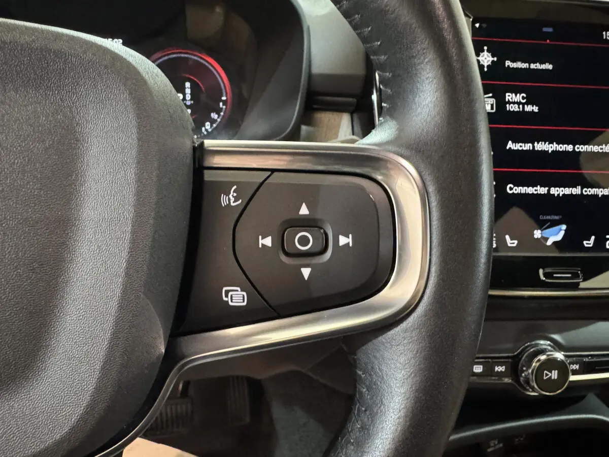 Gros plan sur les commandes au volant côté gauche du Volvo XC40 Recharge T5 noir, avec écran tactile en arrière-plan.