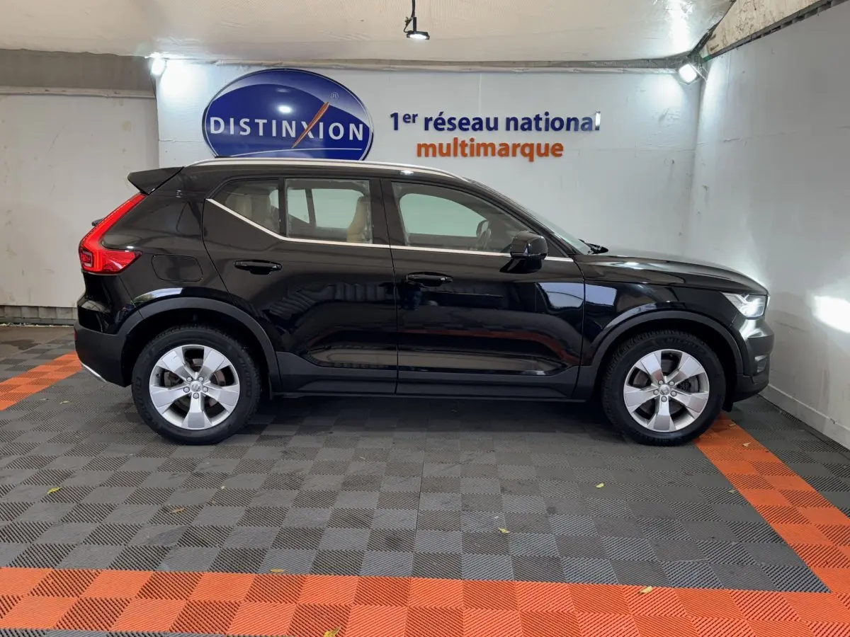 Profil côté gauche d'un Volvo XC40 Recharge T5 noir, avec jantes argentées, stationné en intérieur sur sol gris et orange.