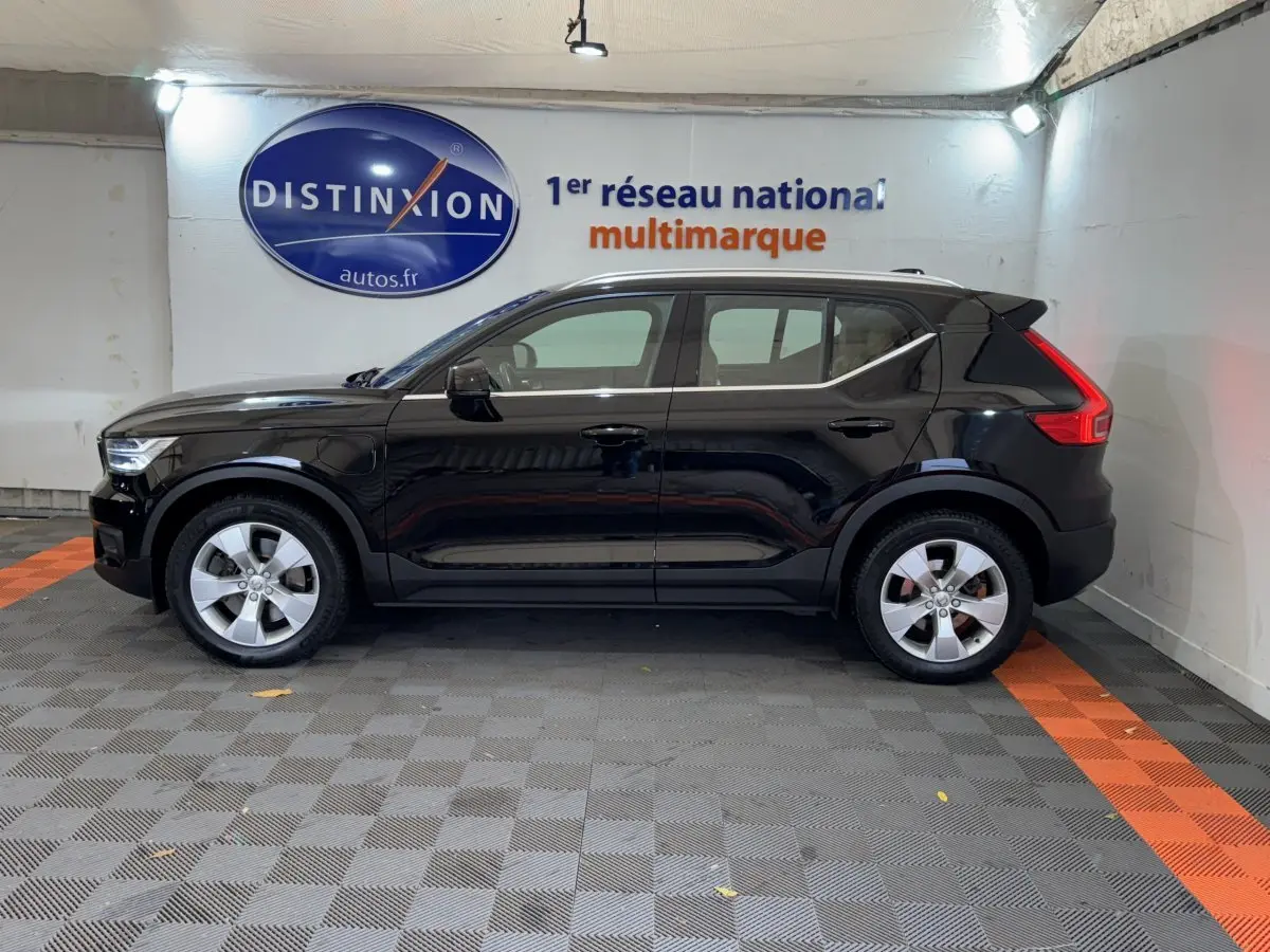 Profil côté gauche d'un Volvo XC40 Recharge T5 noir stationné en intérieur avec jantes argentées et feux arrière distinctifs en L.