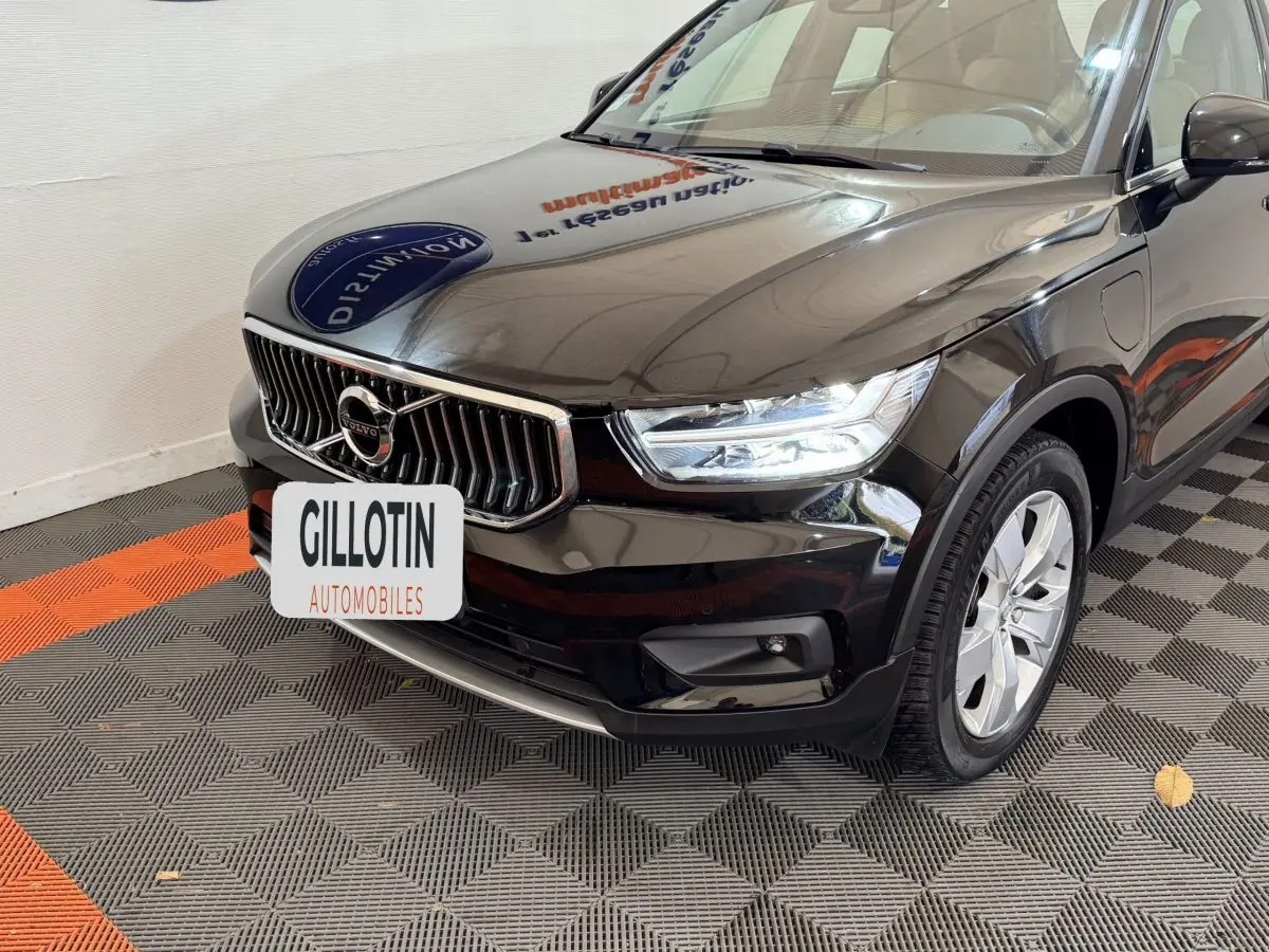 Vue 3/4 avant droit d'un Volvo XC40 noir avec calandre chromée et phares LED allumés en intérieur showroom.