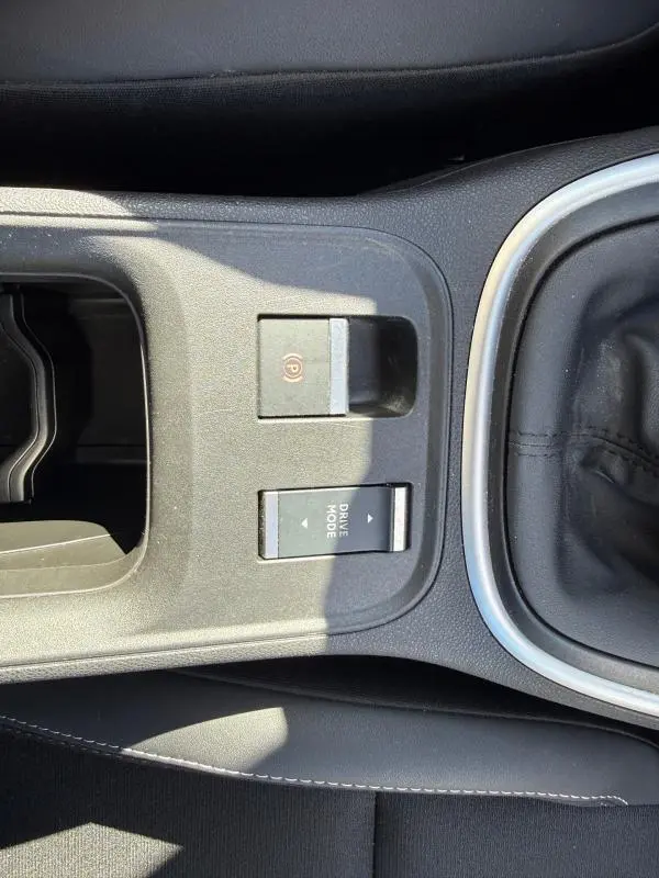 Vue rapprochée de la console centrale noire du Jeep Avenger 2025, montrant le frein à main électrique et le bouton Drive Mode.