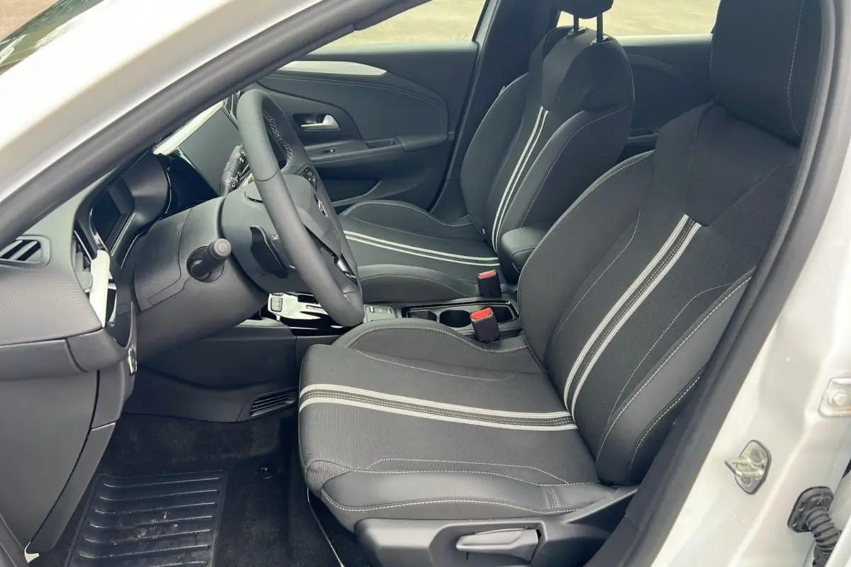 Vue intérieure côté conducteur de l’Opel Corsa blanc kontur, sièges noirs avec surpiqûres claires et volant multifonctions.