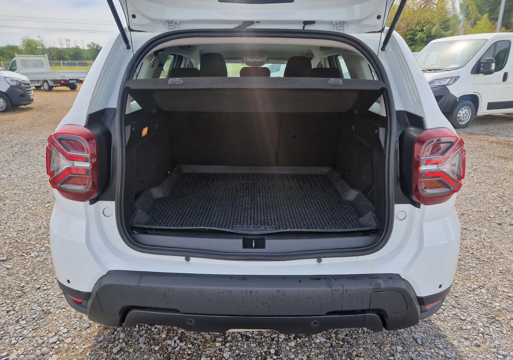 Vue arrière ouverte du coffre d'un Dacia Duster blanc 4x4 2022, avec tapis de protection et hayon relevé.