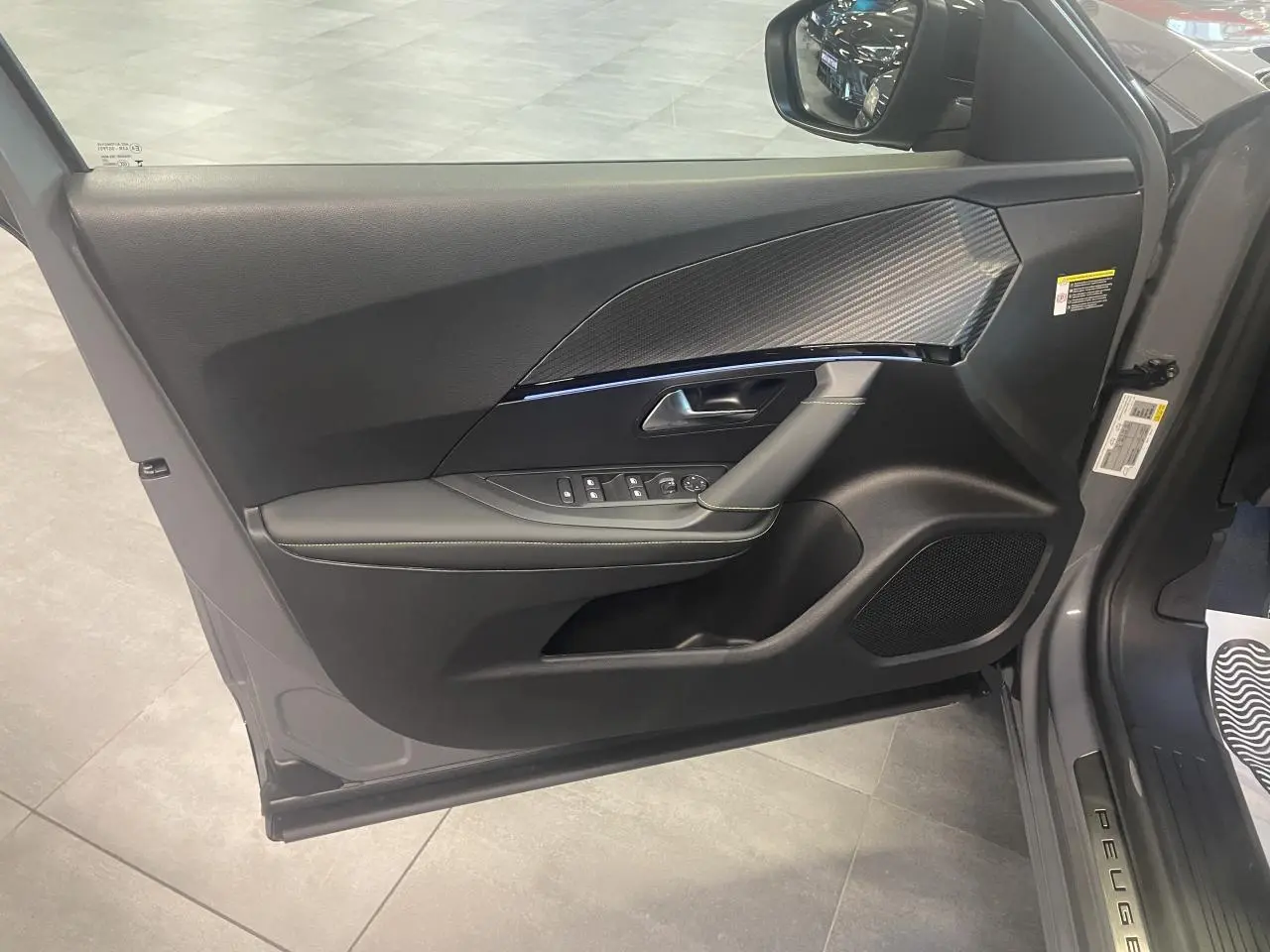 Vue intérieure de la porte avant gauche gris métallisé du Peugeot 2008 1.2i Hybrid GT avec insert carbone et commandes électriques.