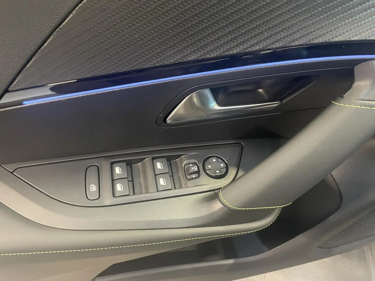 Détail de la porte avant gauche du Peugeot 2008 gris avec surpiqûres vertes et commandes de vitres électriques.