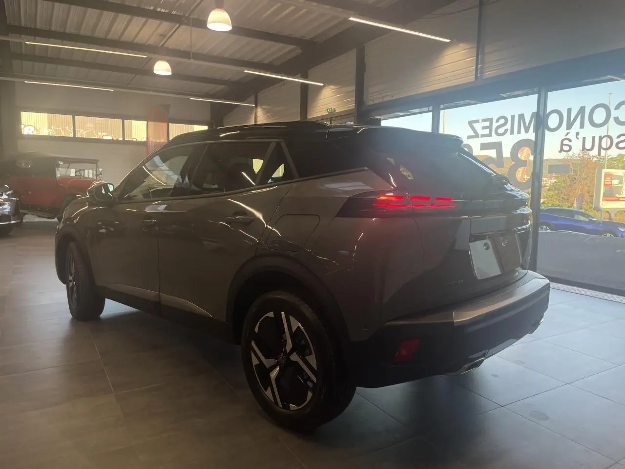Peugeot 2008 gris en 3/4 arrière droit, avec feux arrière LED allumés et jantes au design moderne.