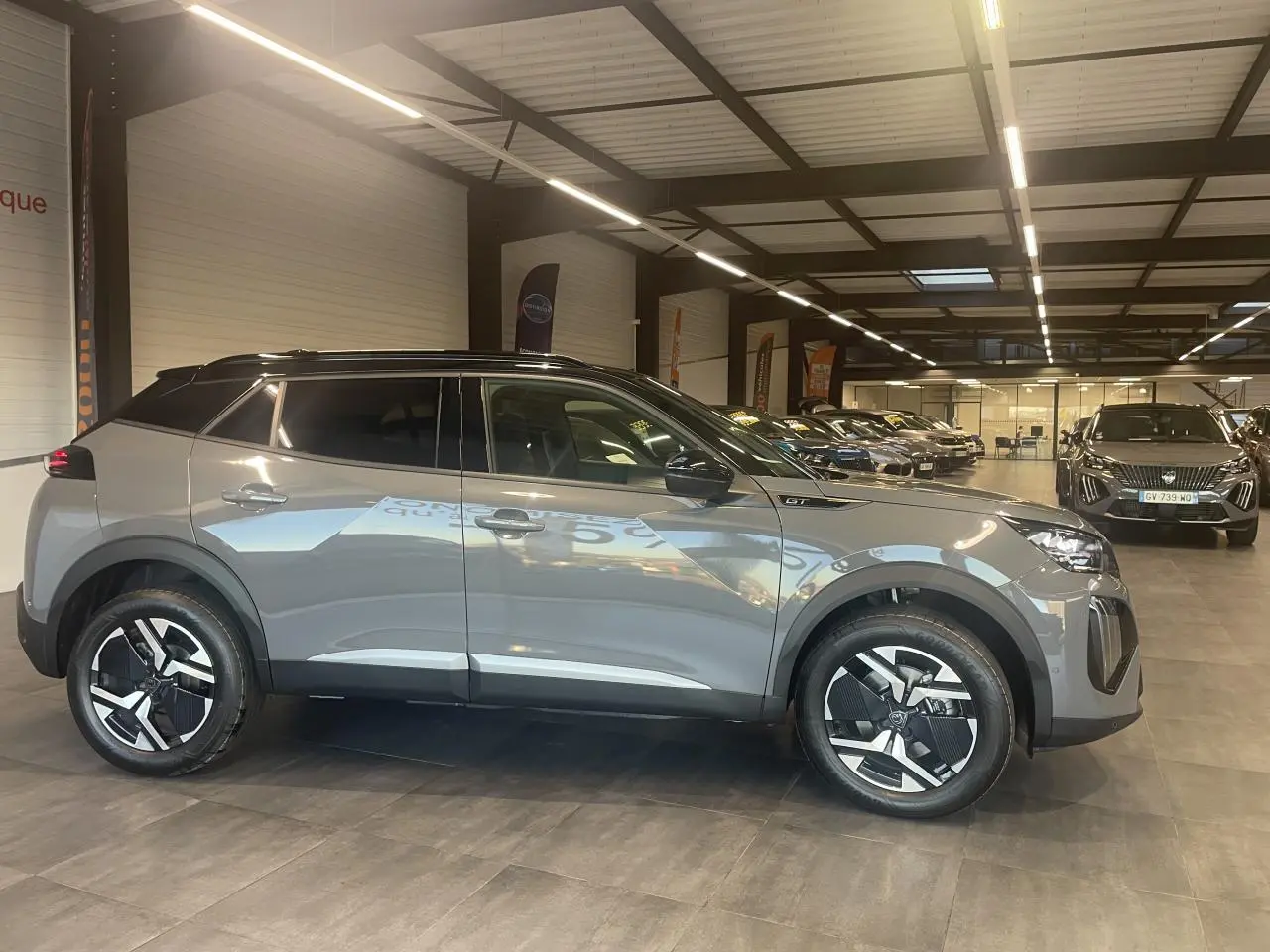 Peugeot 2008 gris métallisé vue de profil côté gauche en intérieur avec toit noir et jantes distinctives.