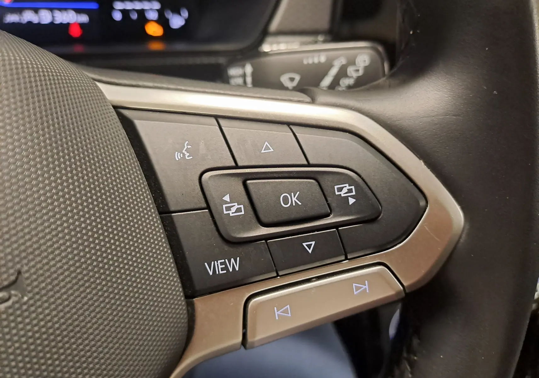 Gros plan sur les commandes au volant du Volkswagen T-Cross 2024, boutons noirs avec cadre argenté.