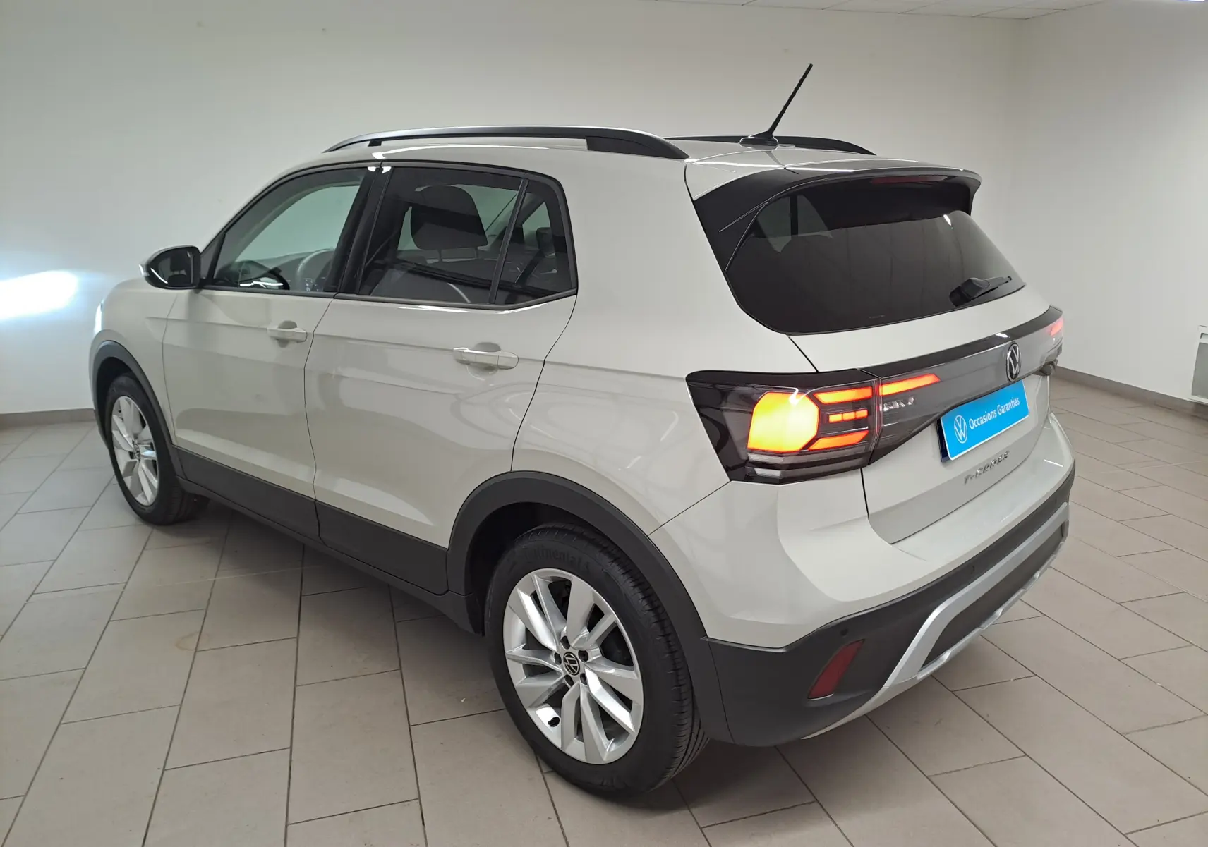 Vue 3/4 arrière droite du Volkswagen T-Cross gris Ascot avec feux arrière allumés en intérieur showroom.
