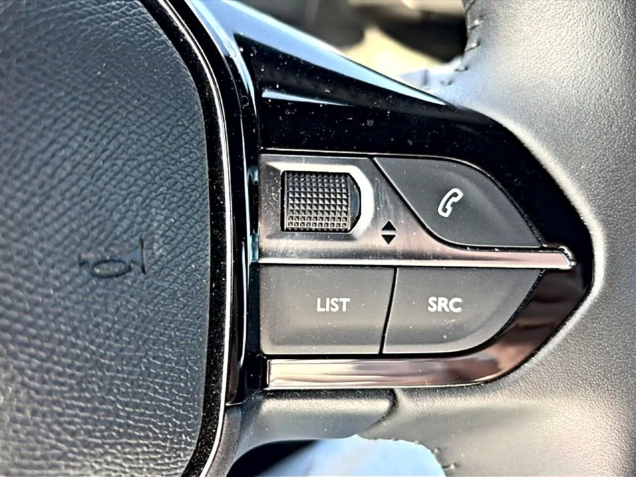 Gros plan sur les commandes gauche du volant noir du Peugeot 2008 gris, boutons LIST et SRC visibles.