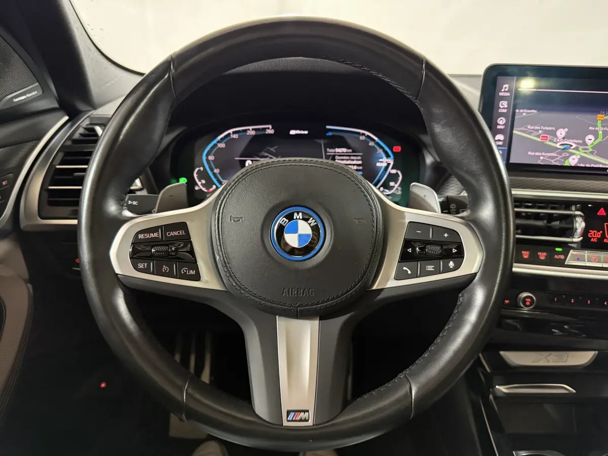 Vue rapprochée du volant cuir noir BMW X3 xDrive30e 2023 avec commandes multifonctions et tableau de bord digital.