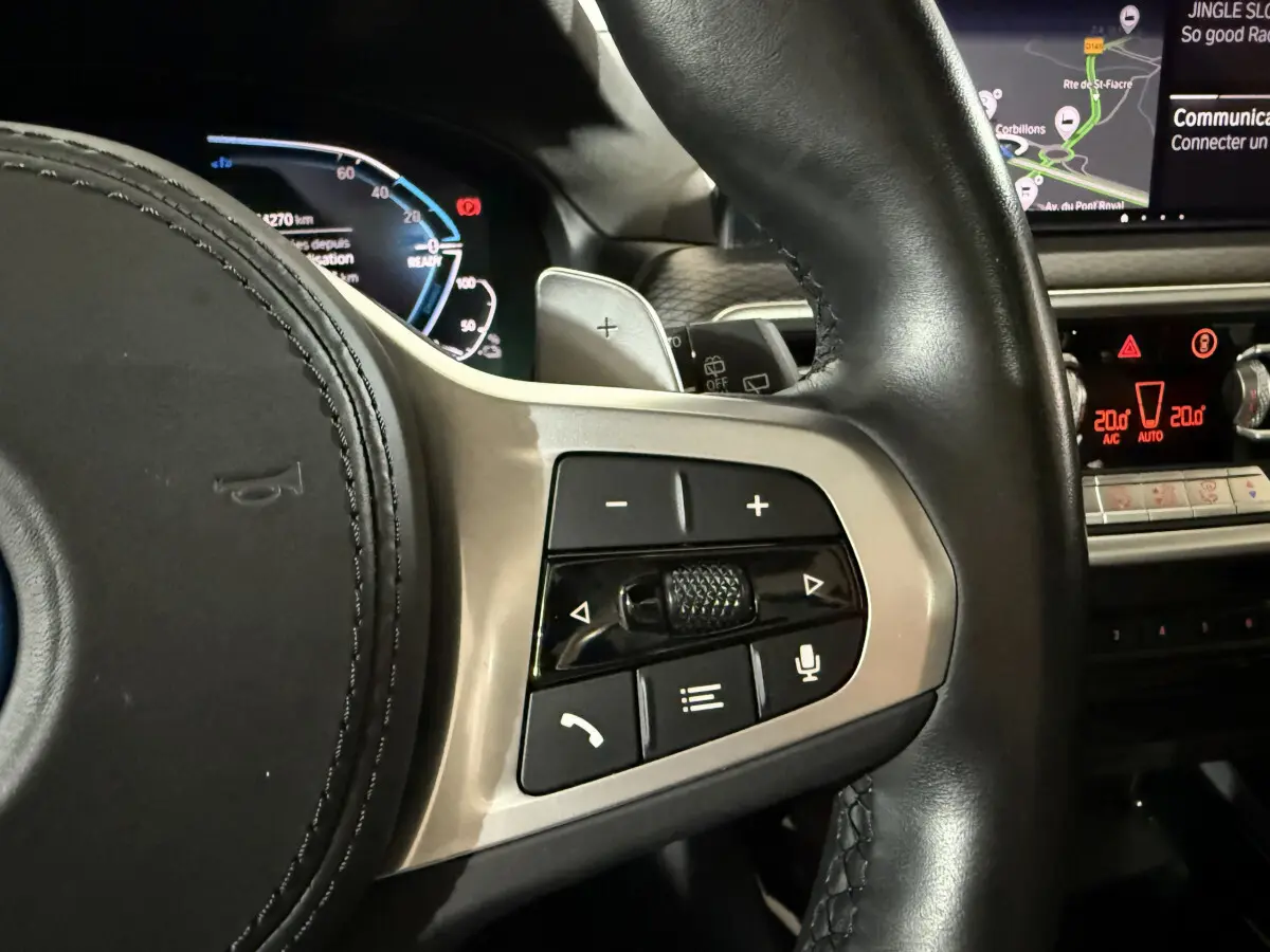 Gros plan sur le côté droit du volant cuir d’un BMW X3 bleu 2023, avec commandes vocales et tableau de bord numérique visible.