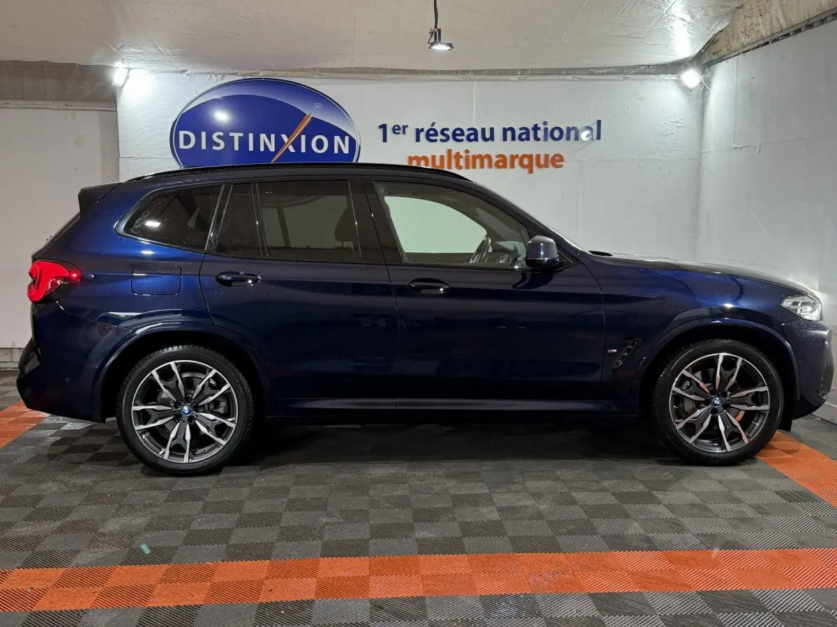 Profil côté gauche d'un BMW X3 xDrive30e bleu 2023 avec jantes alliage et vitres teintées en intérieur showroom.