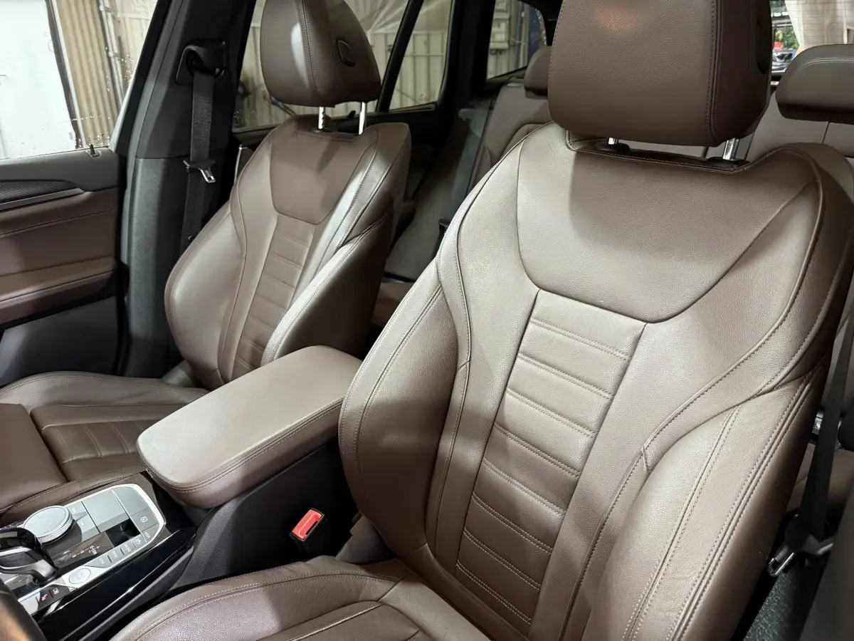 Gros plan sur les sièges avant en cuir marron du BMW X3 xDrive30e 2023, avec console centrale et molette de sélection visibles.
