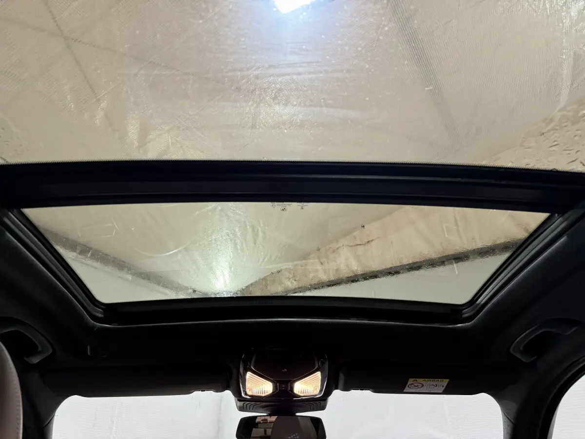 Toit panoramique en verre vu de l'intérieur d'un BMW X3 bleu, éclairage intérieur allumé au centre du plafond.