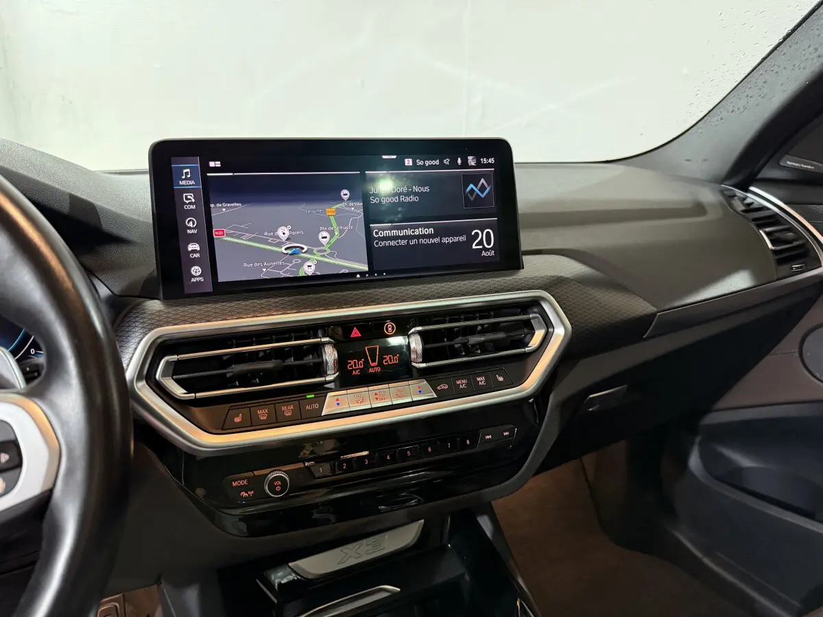 Vue intérieure du tableau de bord du BMW X3 xDrive30e 2023 avec écran tactile 12,3 pouces et commandes climatisation digitales.