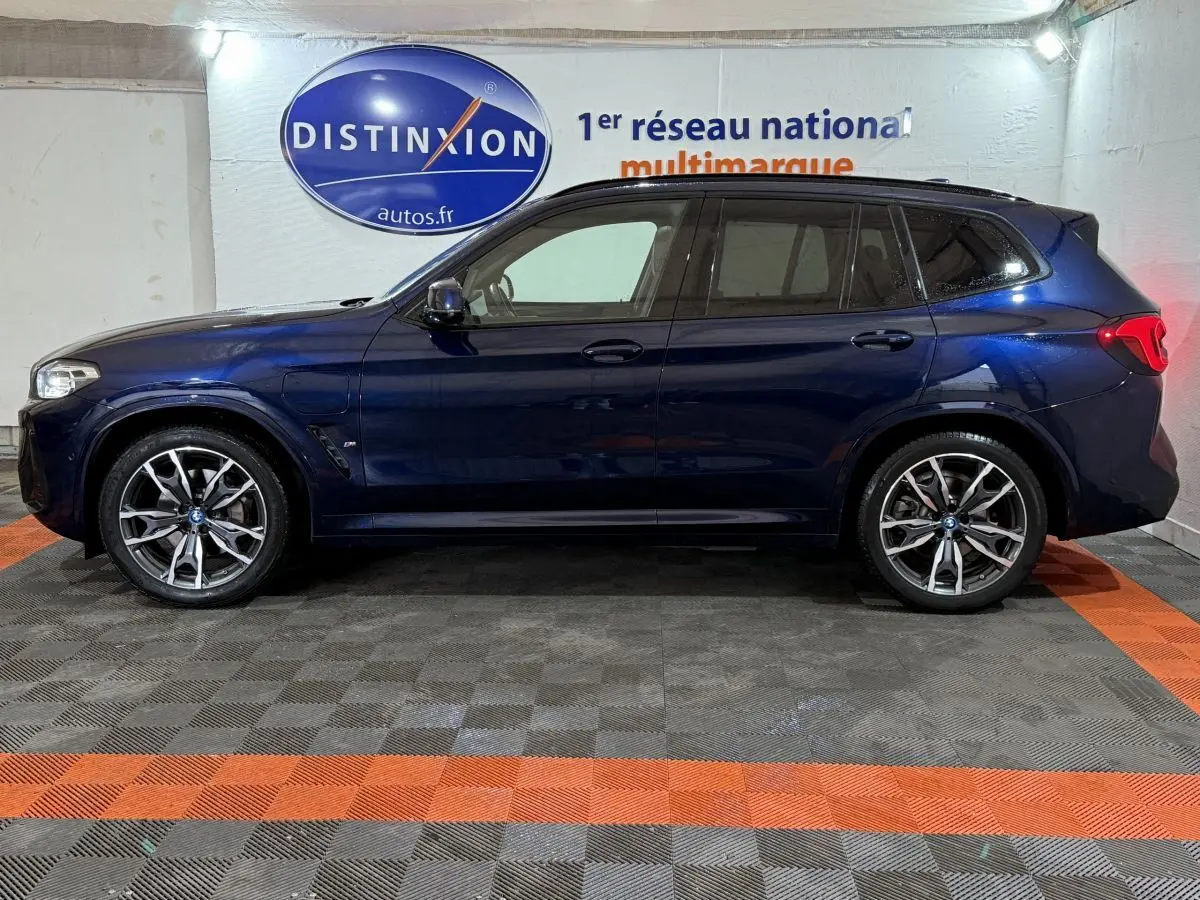 Profil côté gauche d'un BMW X3 xDrive30e bleu 2023 M Sport avec jantes alliage et vitres teintées en intérieur showroom.