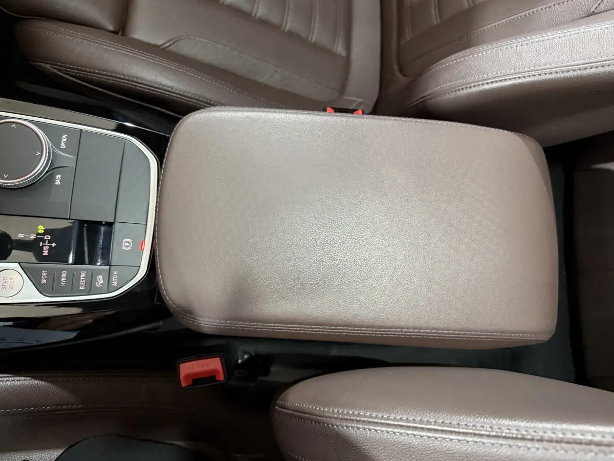 Vue plongeante sur l'accoudoir central en cuir marron et la console de commande du BMW X3 xDrive30e 2023 M Sport.