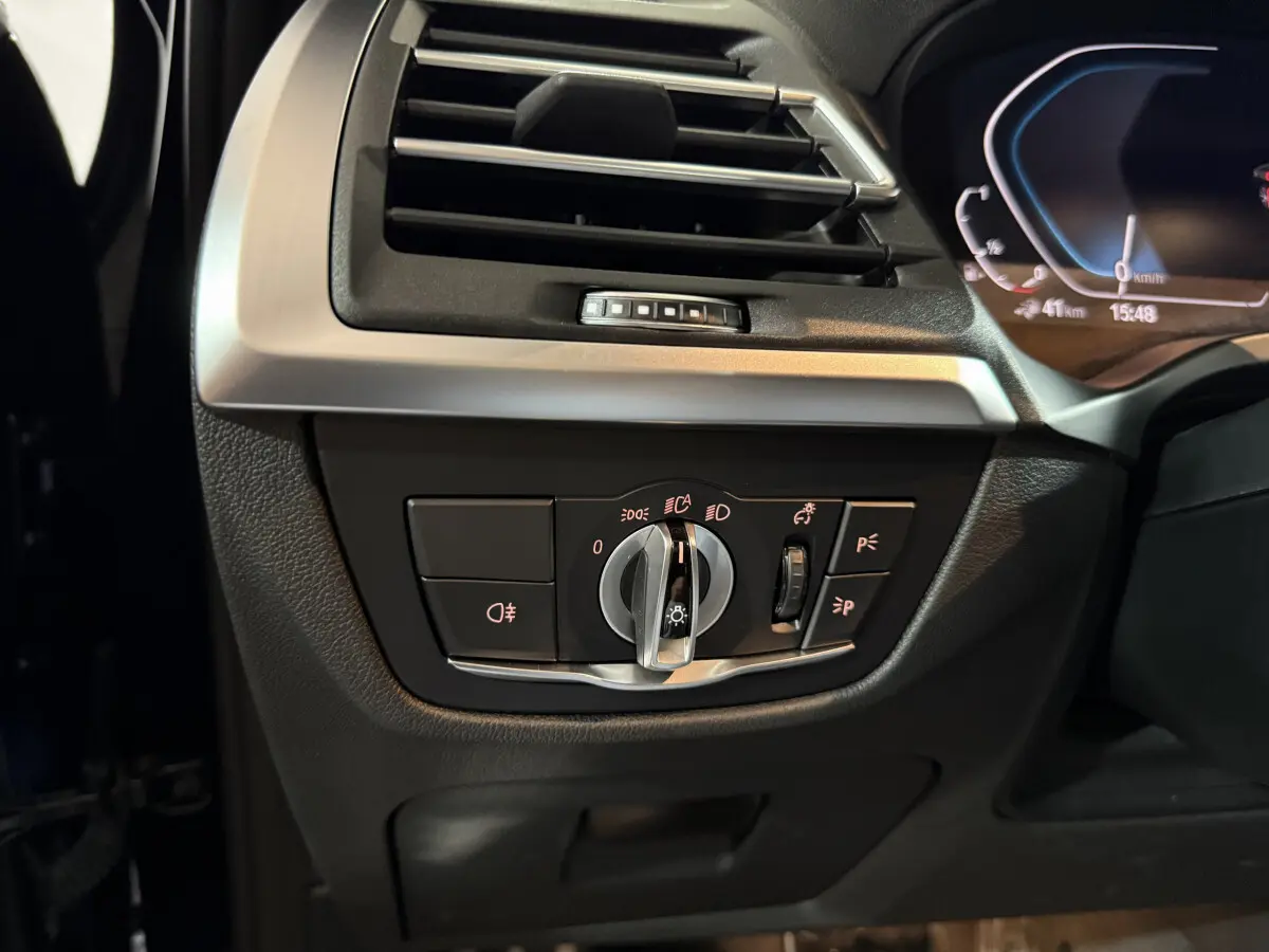 Gros plan sur la commande des phares et la sortie d'air côté gauche du tableau de bord d'un BMW X3 bleu 2023.