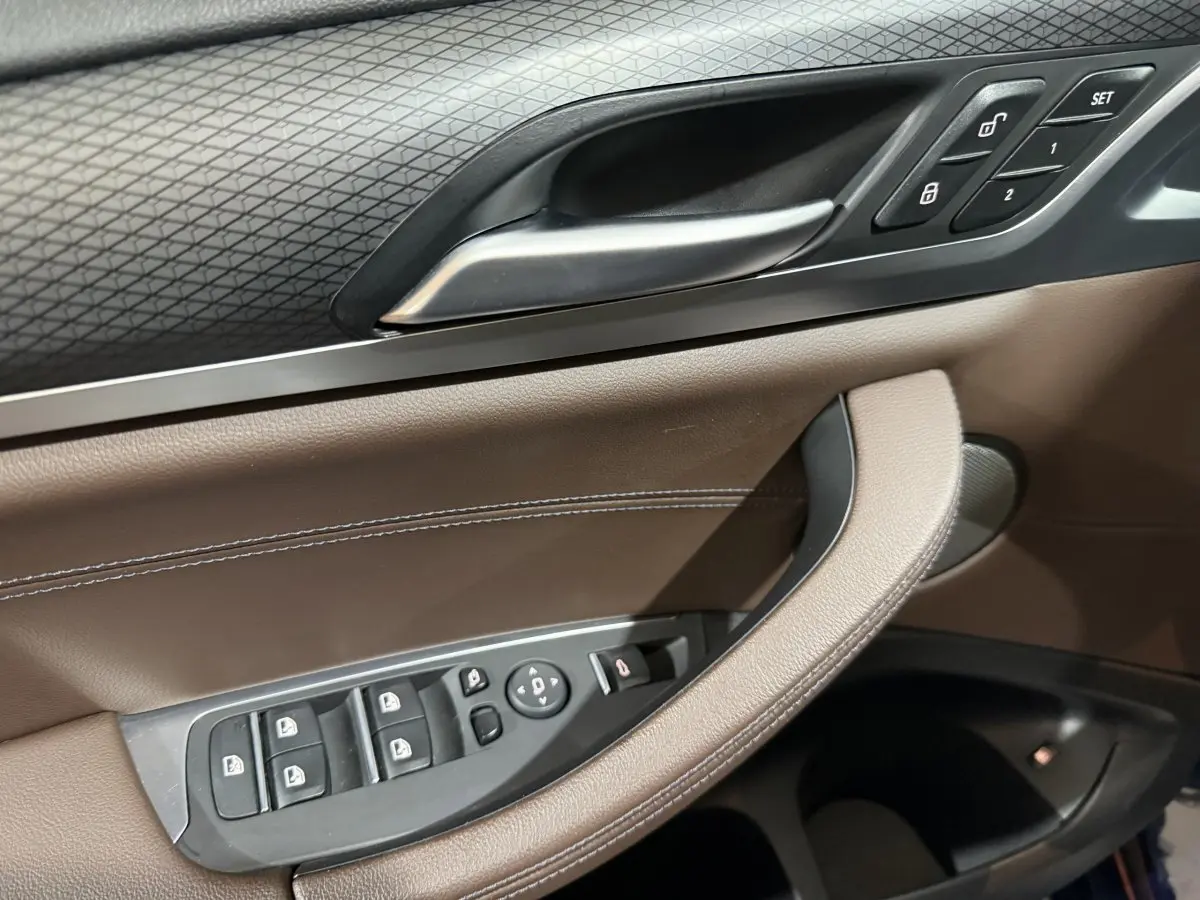 Gros plan sur la porte côté conducteur du BMW X3 bleu 2023, montrant les commandes des vitres et la poignée en cuir marron.