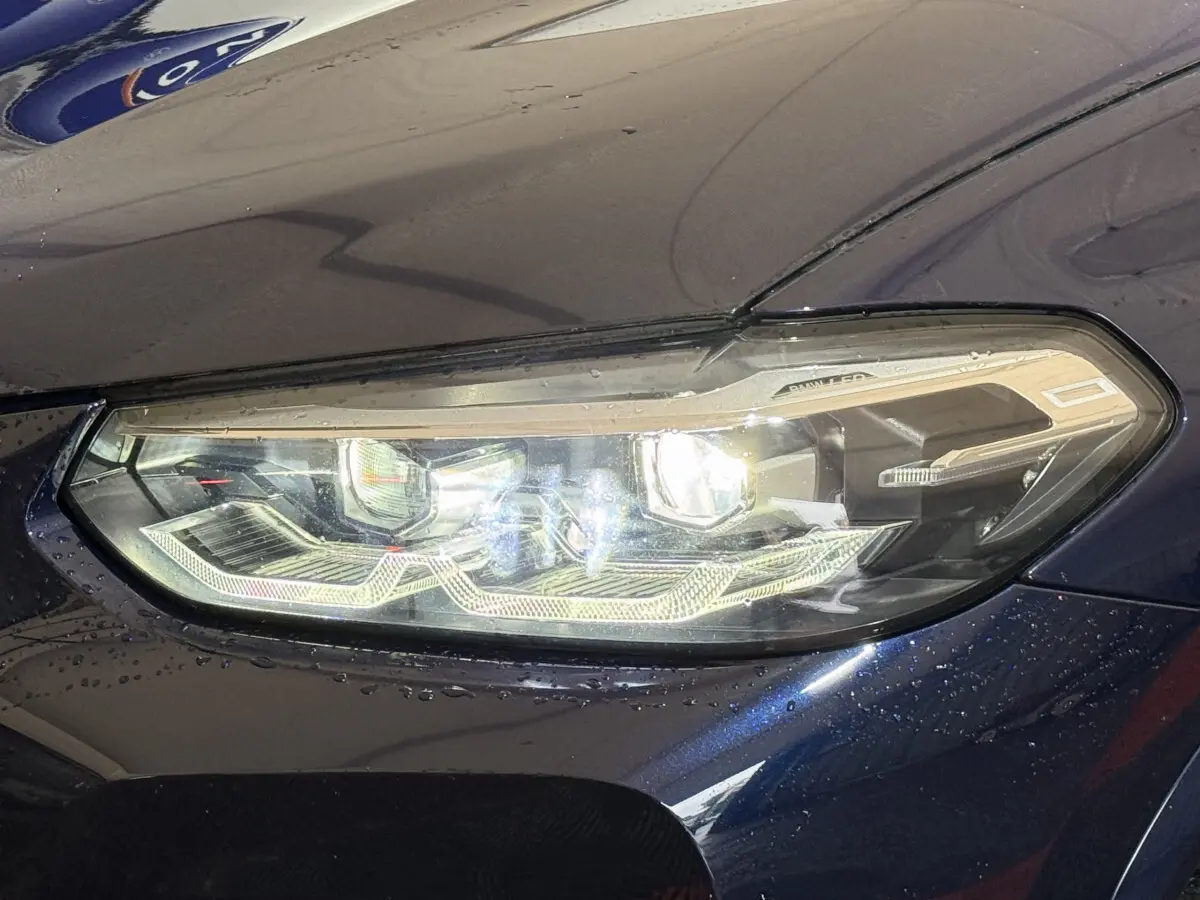 Gros plan sur le phare avant droit allumé d'un BMW X3 xDrive30e bleu 2023 avec détails LED distinctifs.