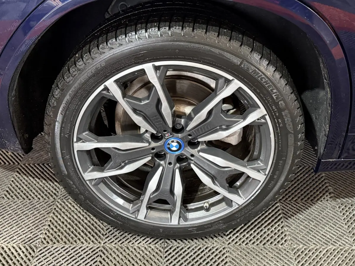 Gros plan sur la roue avant gauche du BMW X3 xDrive30e bleu 2023 avec jante alu M Sport au design moderne.