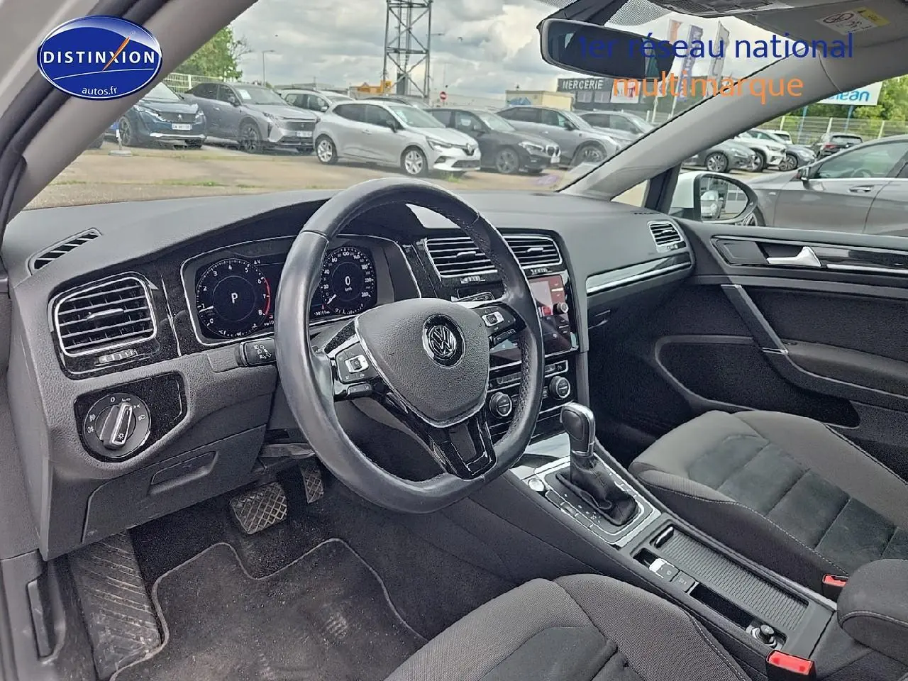 Vue intérieure côté conducteur de la Volkswagen Golf blanche, montrant le volant cuir multifonction et la console centrale.