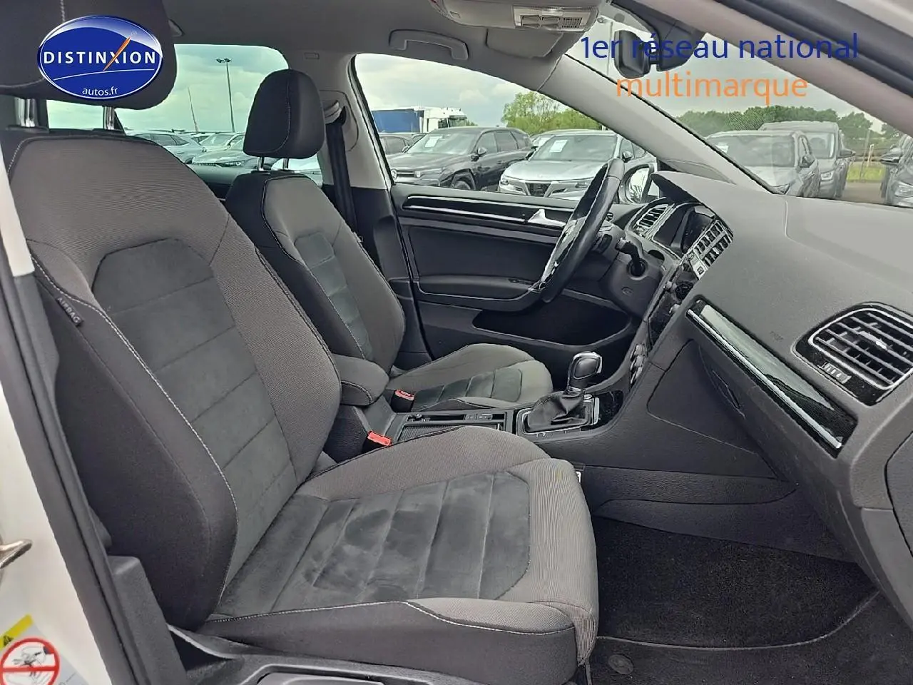 Vue intérieure côté conducteur de la Volkswagen Golf blanche, montrant les sièges tissu gris et le tableau de bord.