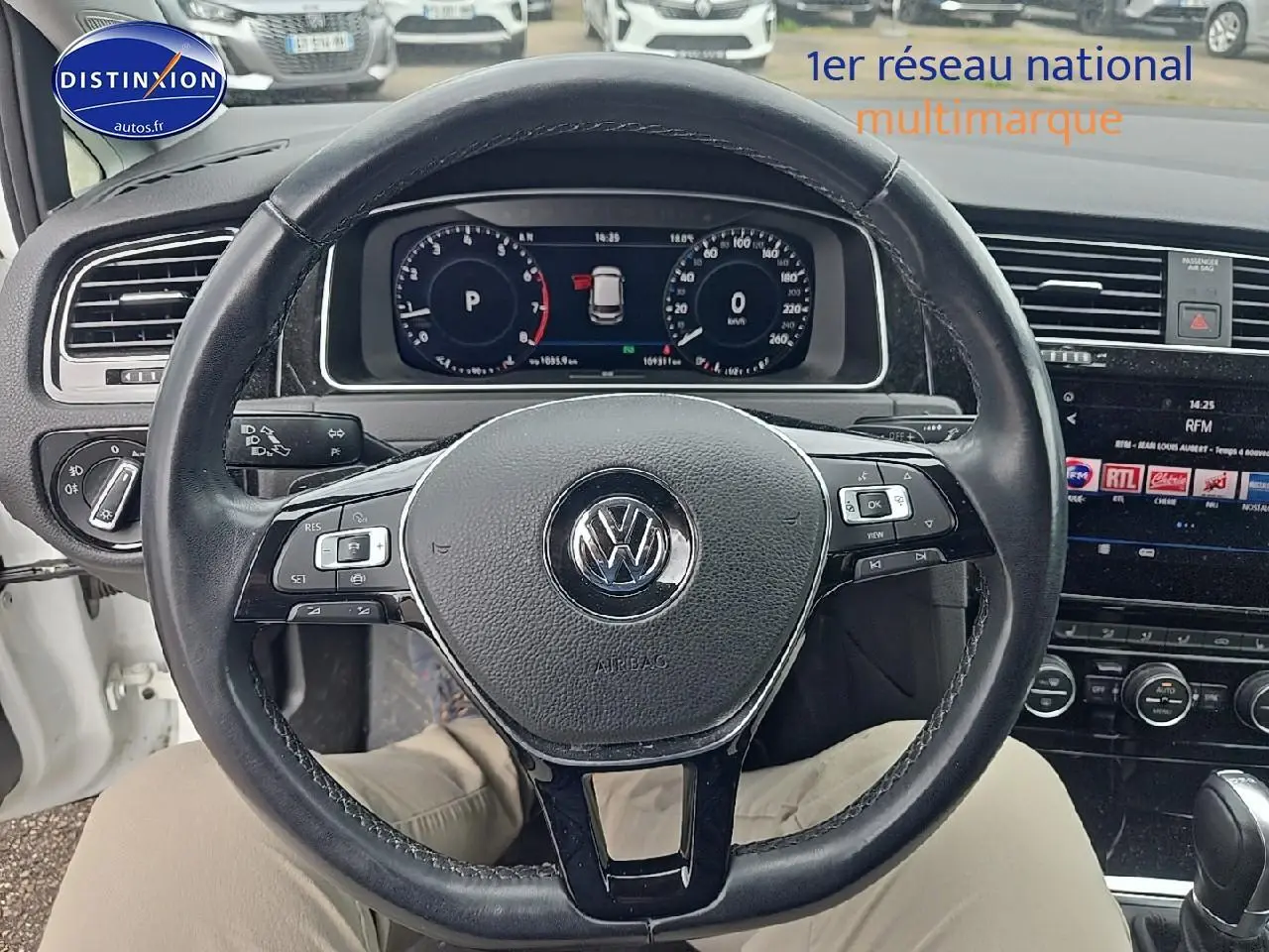 Vue intérieure centrée sur le volant cuir noir d'une Volkswagen Golf blanche, avec tableau de bord digital et écran tactile visible.