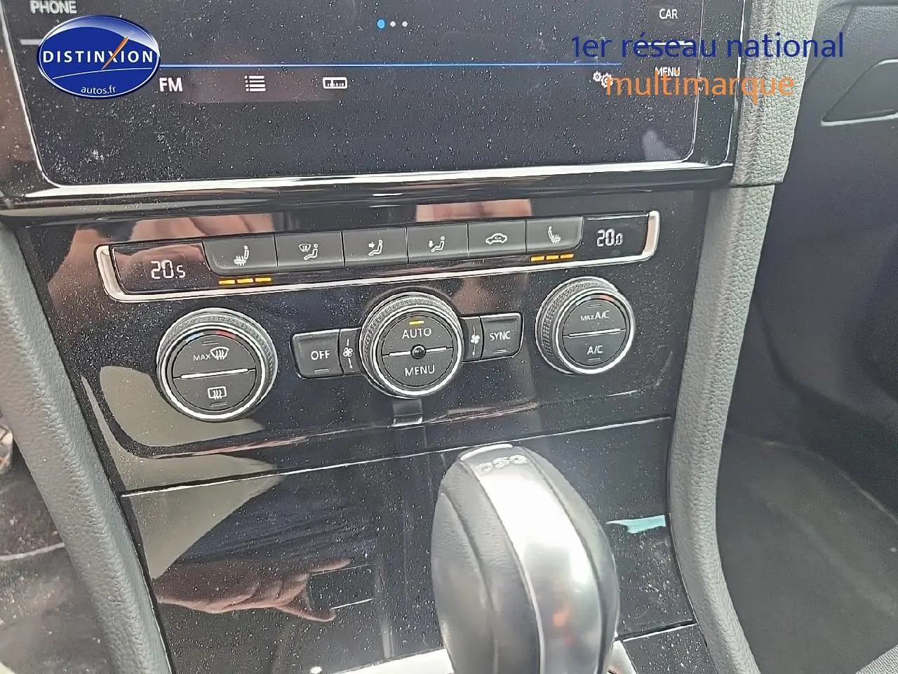 Vue rapprochée de la console centrale noire avec commandes climatisation et levier de vitesse DSG d’une Volkswagen Golf blanche.