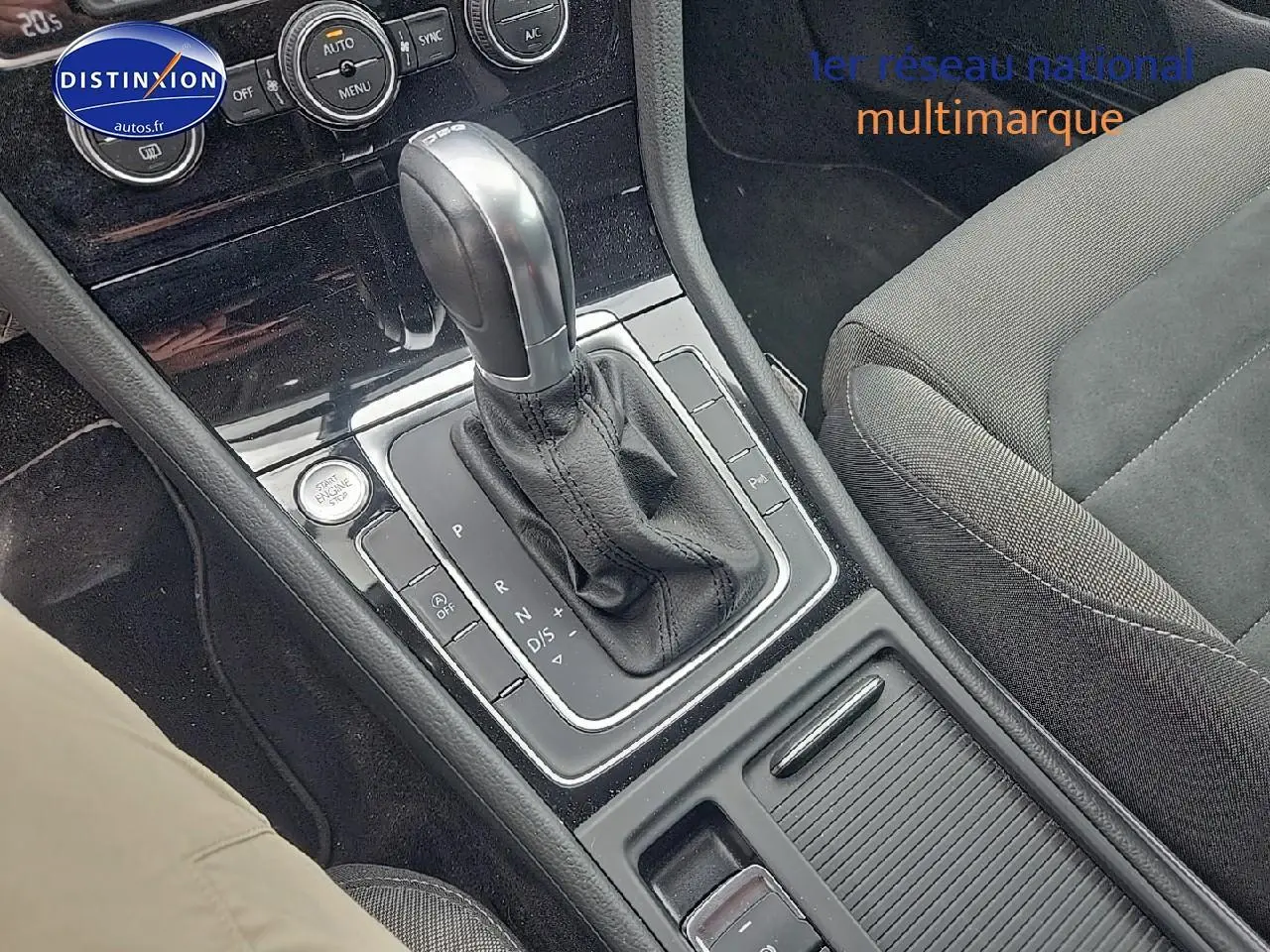 Gros plan sur la console centrale avec levier de boîte auto et siège tissu gris côté droit d’une Volkswagen Golf blanche.