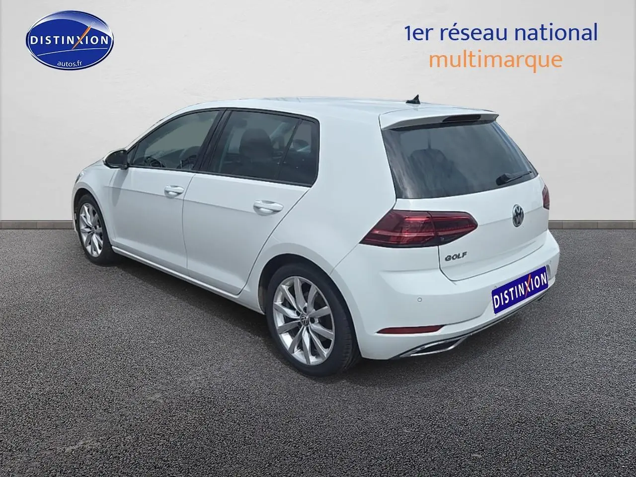 Vue 3/4 arrière droite d'une Volkswagen Golf blanche avec jantes alu et vitres teintées sur fond neutre.