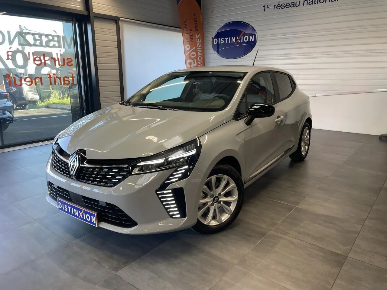 Renault Clio 1.5 Blue dCi 2025 gris Rafale vue 3/4 avant en intérieur avec feux LED et jantes alliage.