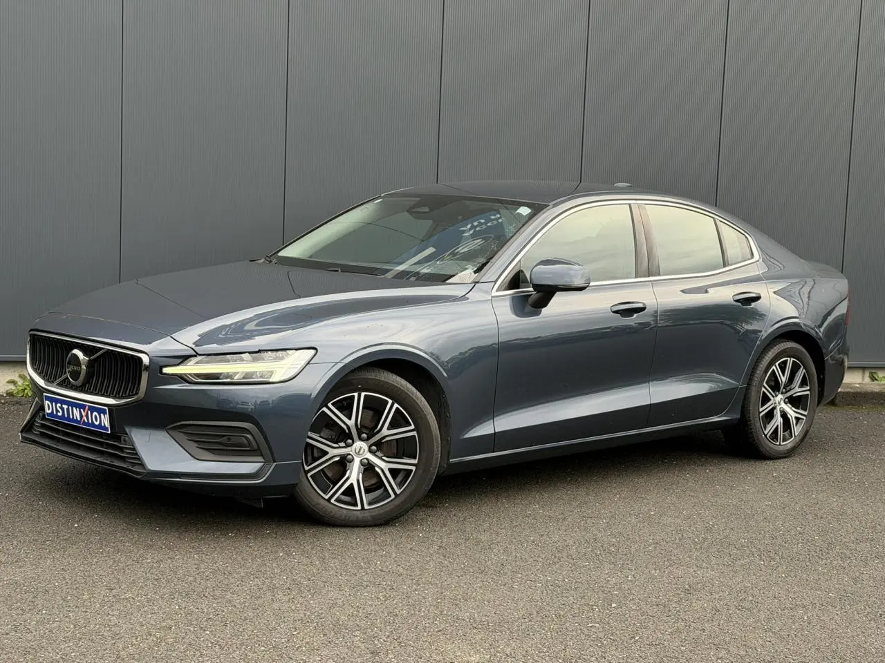 Volvo S60 gris Denim vue 3/4 avant droit, avec jantes alliage 17 pouces et contours de fenêtres chromés.