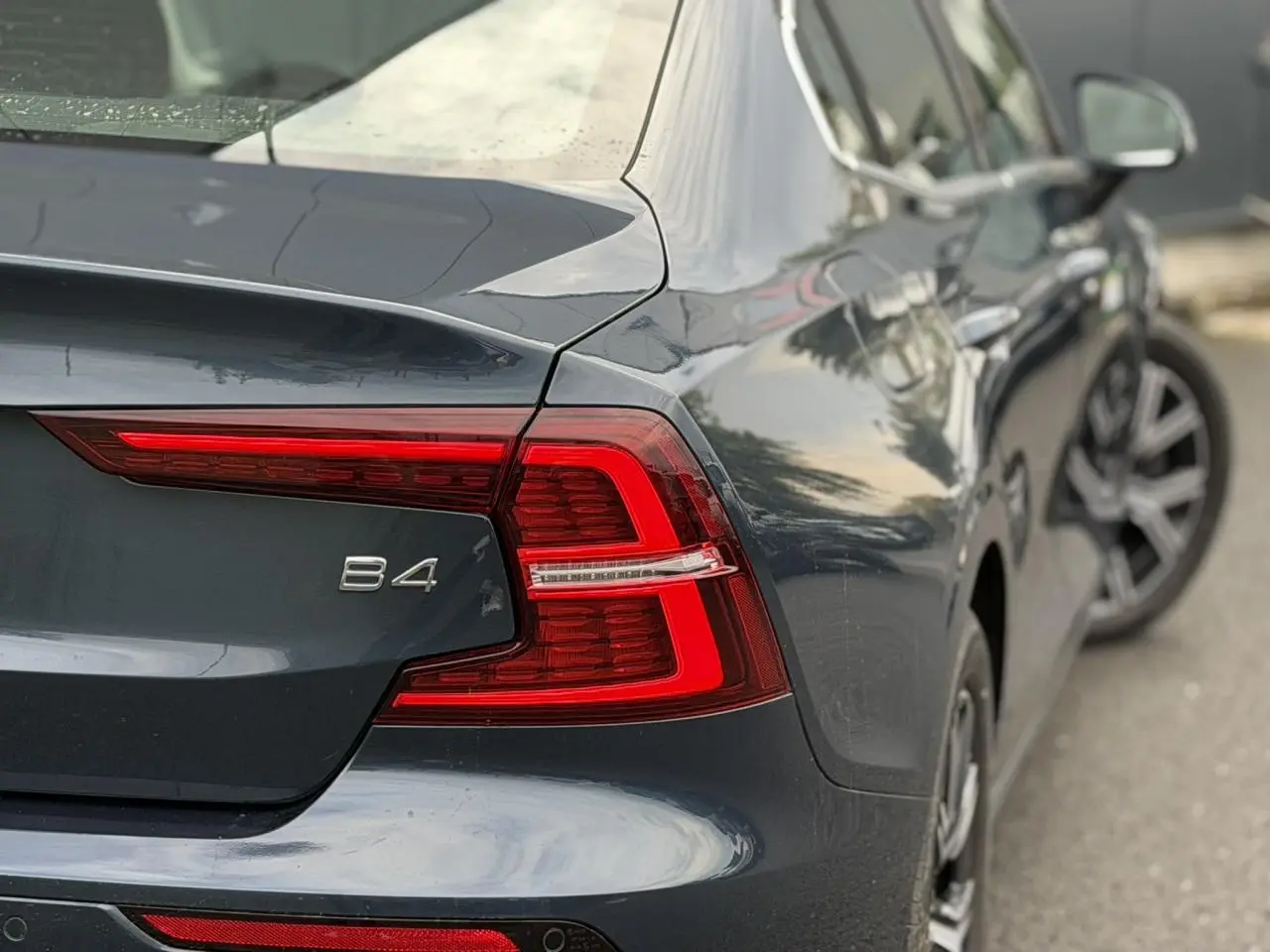 Vue 3/4 arrière droite d'une Volvo S60 B4 gris Denim avec feux arrière LED et jantes alliage 17 pouces.