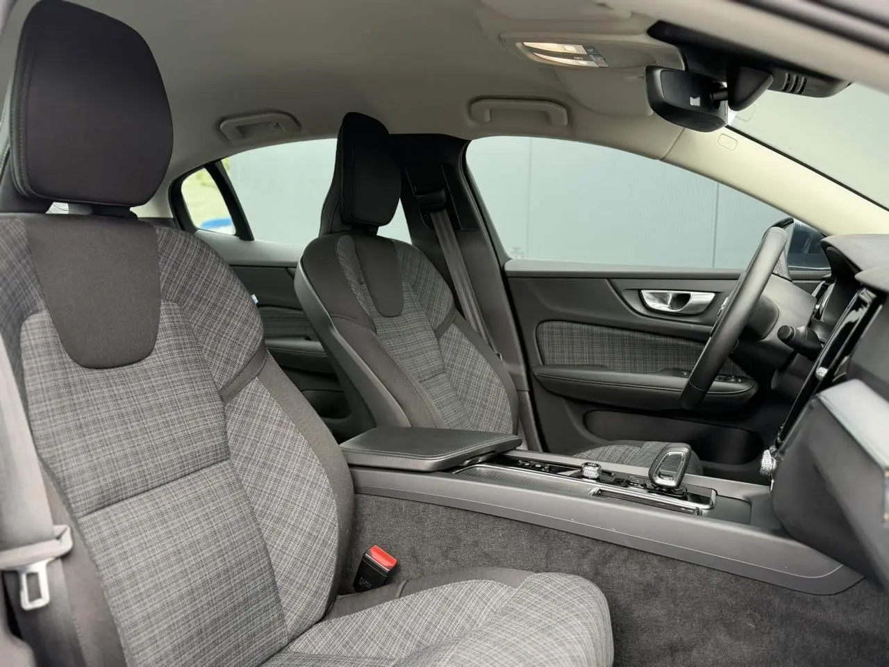 Vue intérieure côté droit de la Volvo S60 2024, sièges tissu gris à motif écossais avec console centrale et volant visibles.