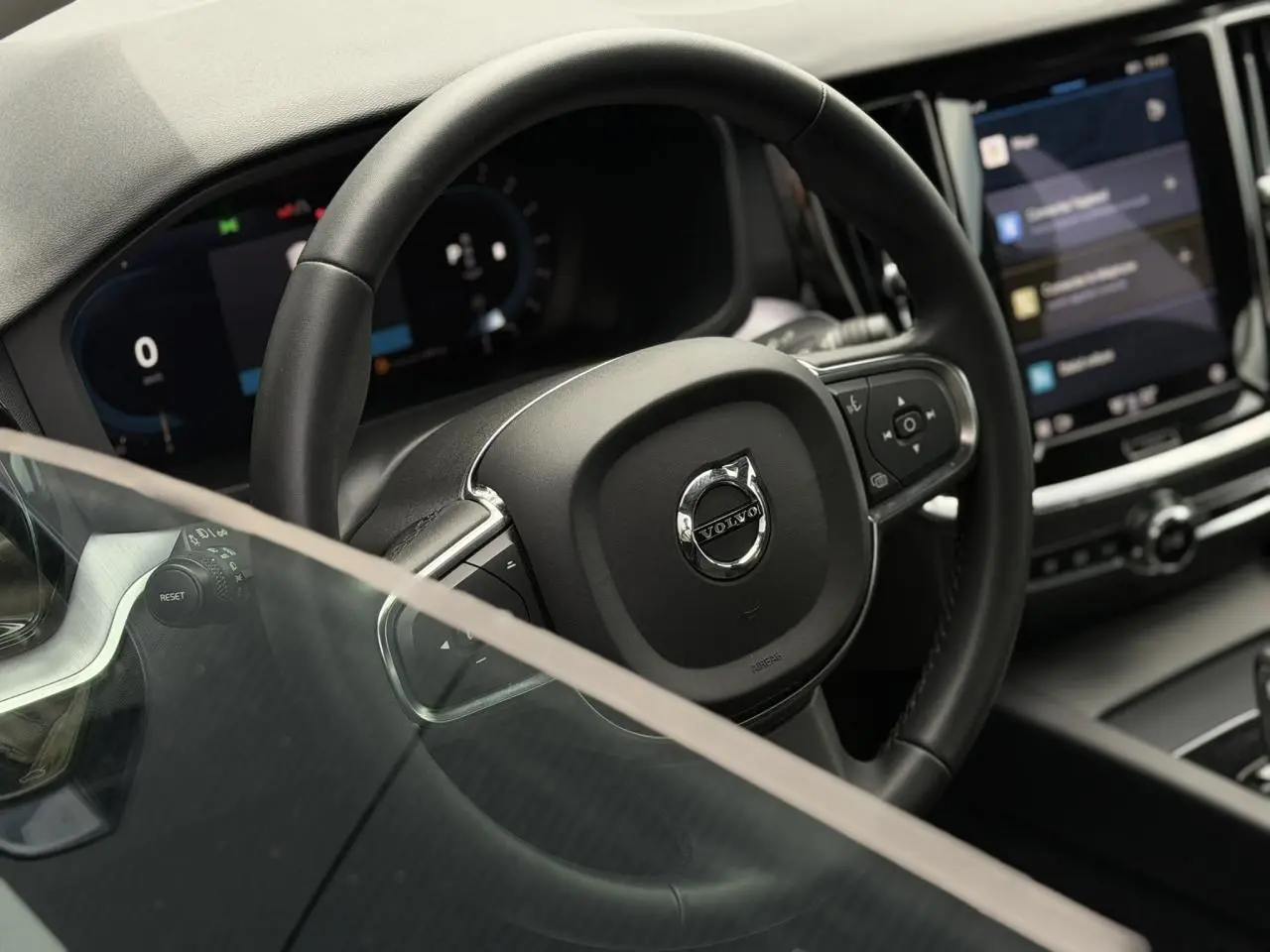 Vue rapprochée du volant noir et du tableau de bord numérique de la Volvo S60 2024, avec écran tactile central visible.