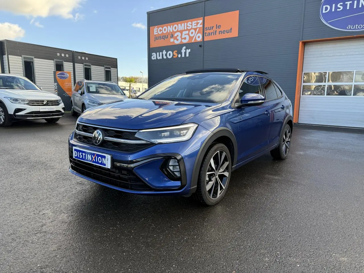 Volkswagen Taigo bleu récif métallisé en 3/4 avant droit avec jantes alliage noires brillantes sur parking.