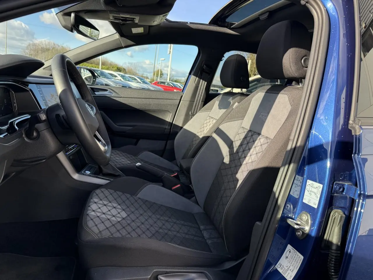 Intérieur côté conducteur du Volkswagen Taigo bleu récif, sièges tissu noir et gris avec motifs géométriques.