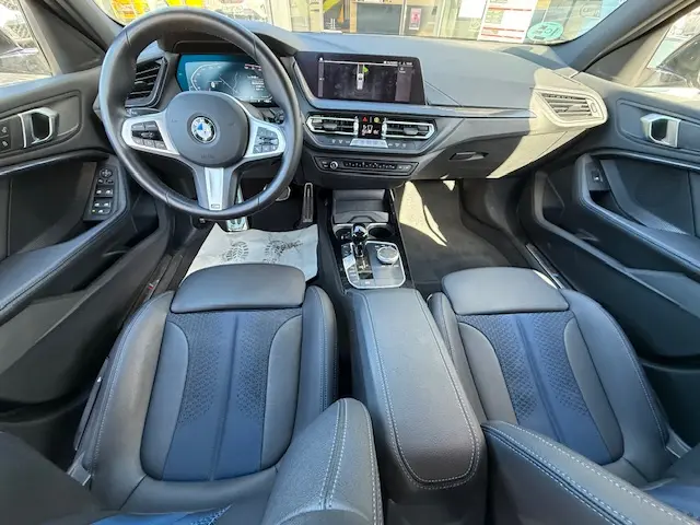 Vue intérieure avant de la BMW Série 1 118d Edition Sport 2024, sièges cuir noirs et tableau de bord avec écran tactile.