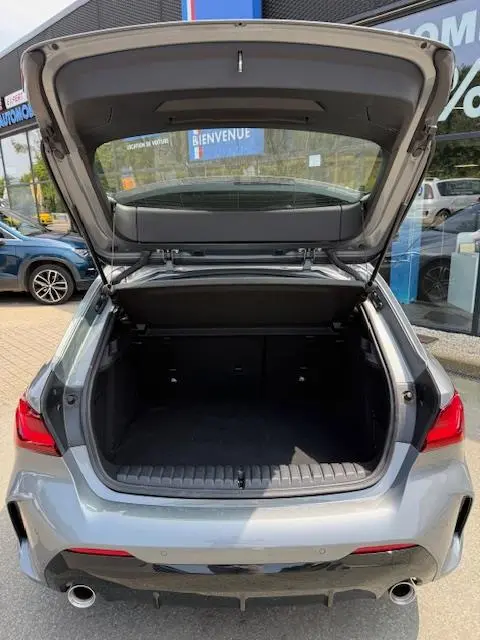 Vue arrière ouverte sur le coffre spacieux d'une BMW Série 1 118d gris foncé avec feux LED et double sortie d'échappement.