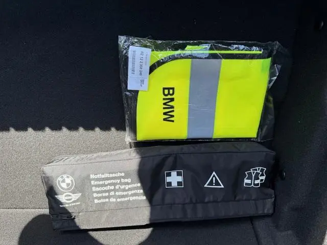 Gilet de sécurité jaune fluo BMW et trousse d'urgence noire posés dans le coffre d'une BMW Série 1 gris foncé.