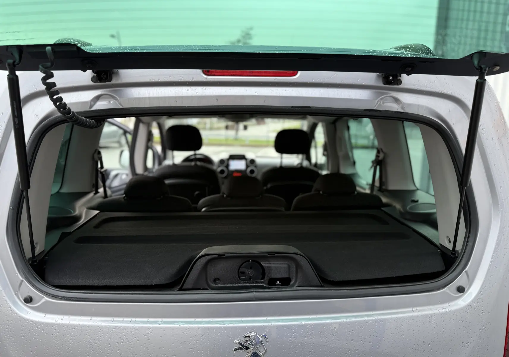 Vue arrière du Peugeot Partner Tepee gris 2018 avec hayon ouvert, montrant l'intérieur et les sièges arrière.