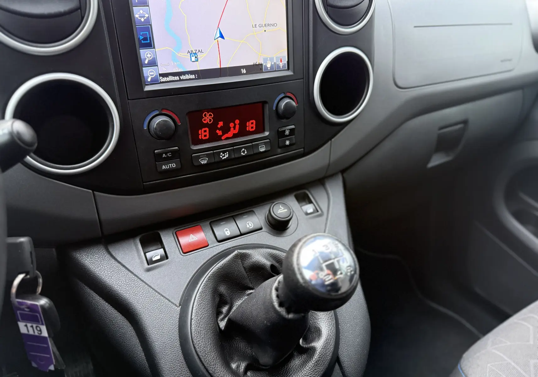 Vue intérieure du tableau de bord et levier de vitesses manuel du Peugeot Partner Tepee gris, avec écran de navigation et commandes climatisation.