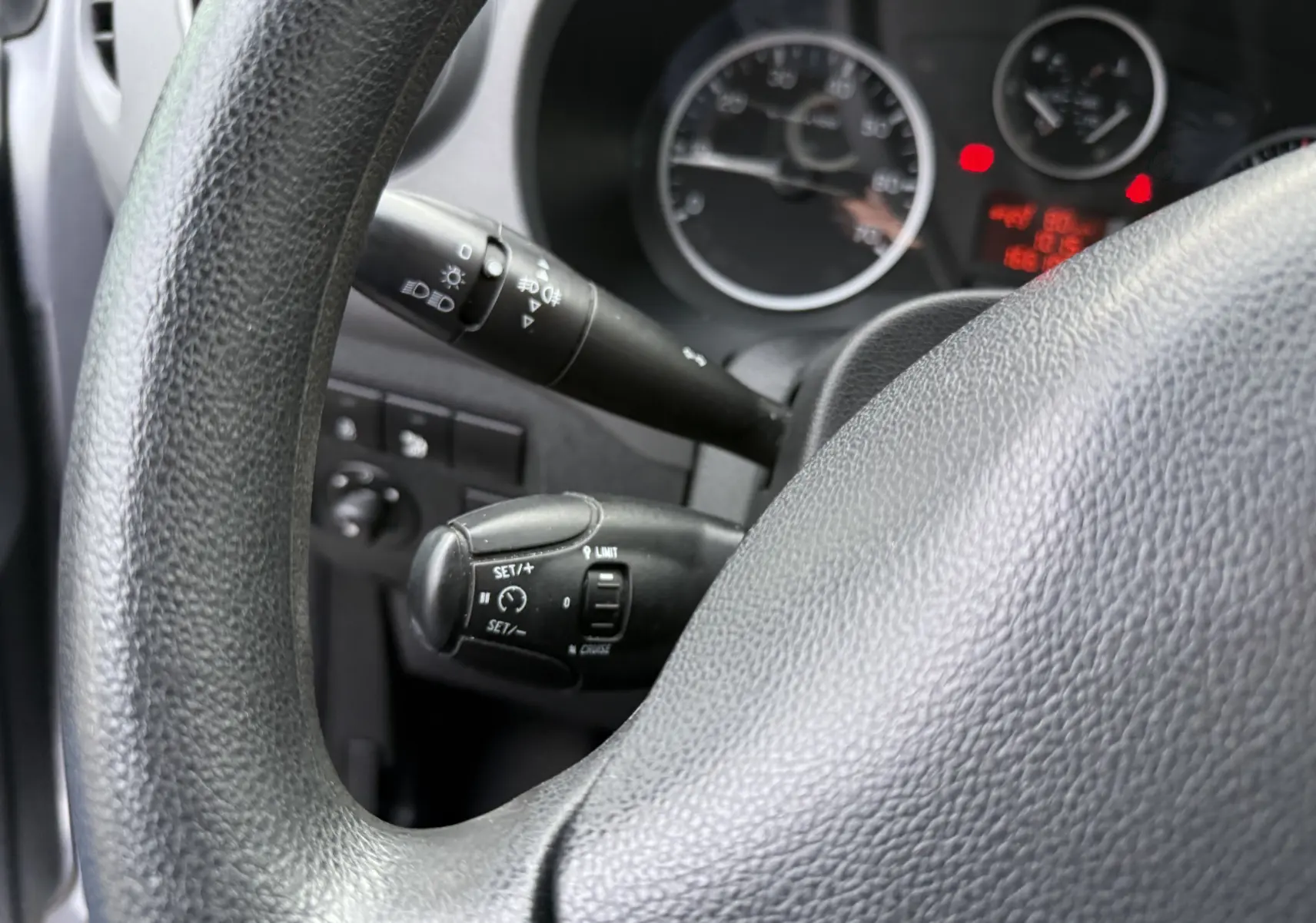 Gros plan sur le volant noir et les commandes de régulateur de vitesse du tableau de bord du Peugeot Partner Tepee gris.