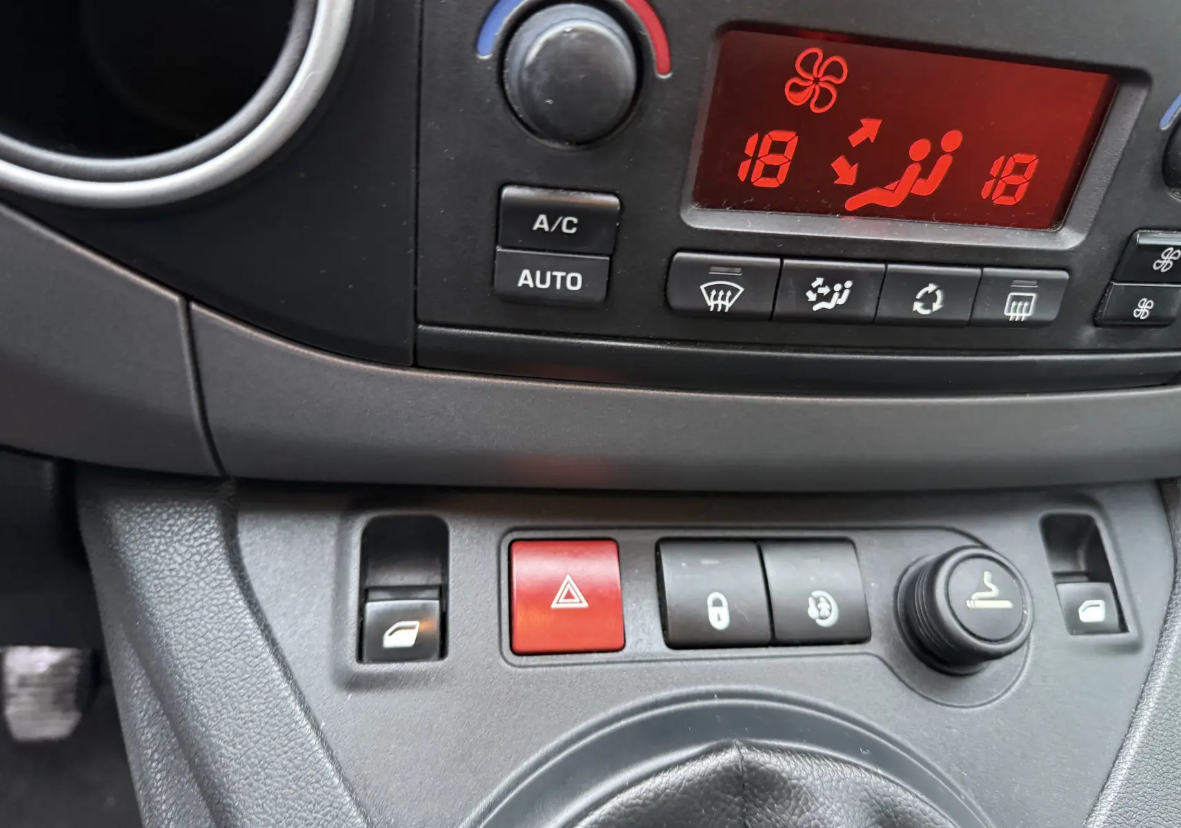 Vue rapprochée du tableau de bord gris du Peugeot Partner Tepee 2018, montrant les commandes de climatisation et les boutons de sécurité.