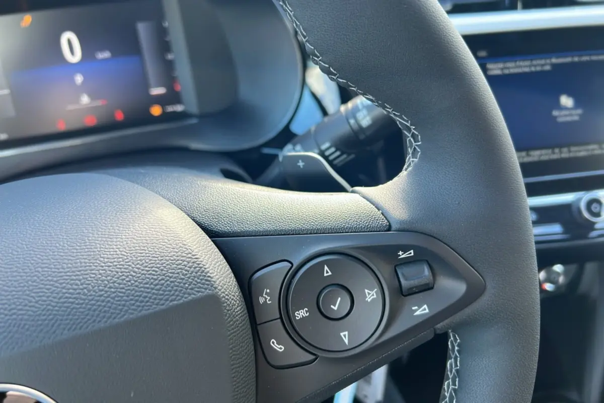 Gros plan sur les commandes multifonctions du volant cuir noir de l’Opel Corsa Hybrid 110 e-DCT6, intérieur moderne.