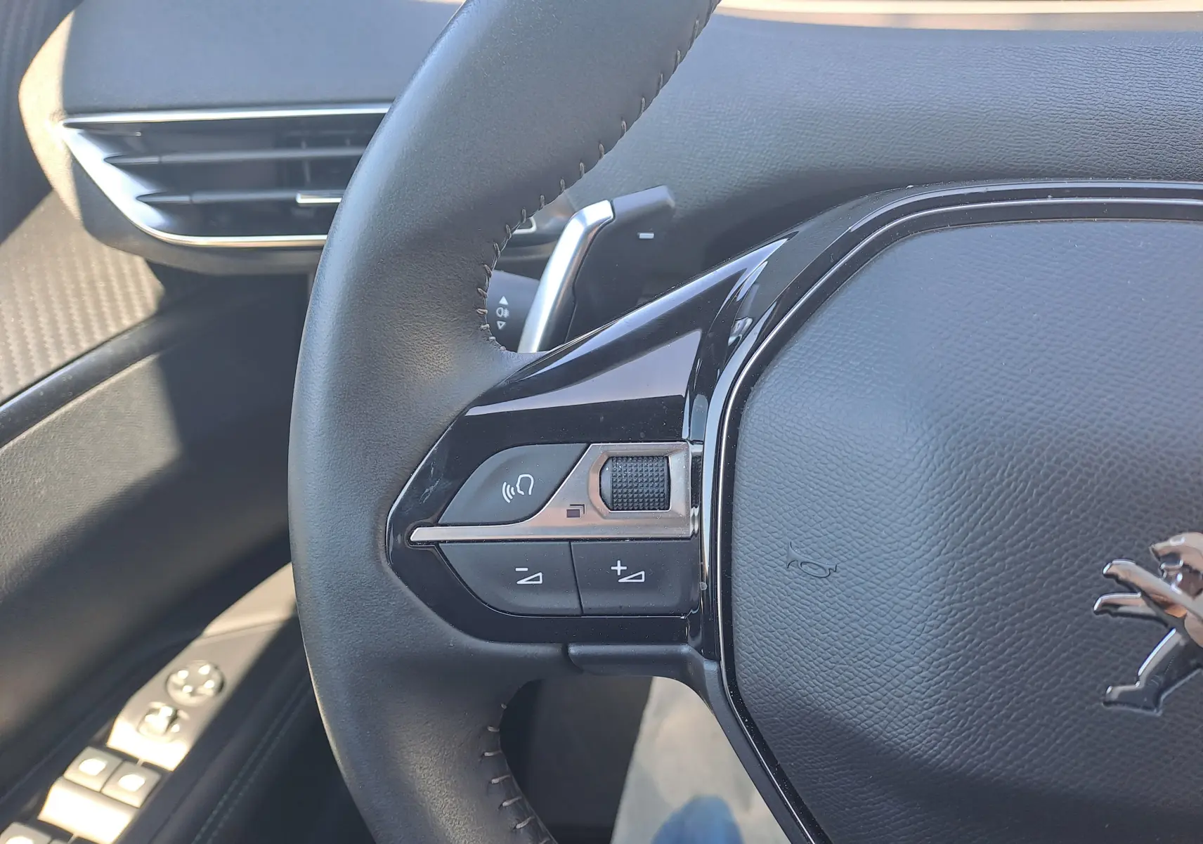 Gros plan sur le volant noir du Peugeot 3008 2023, montrant les commandes audio et le logo lion chromé.