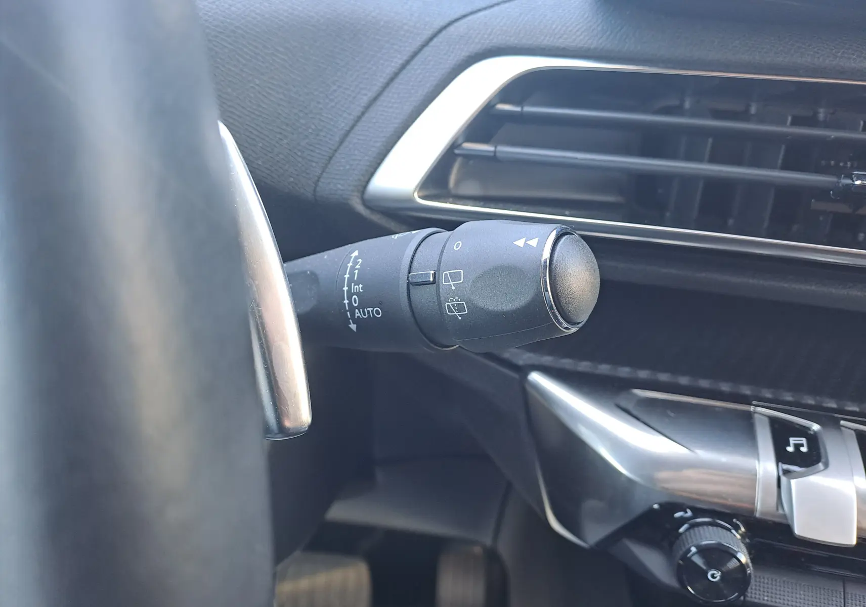 Gros plan sur la commande d’essuie-glace à gauche du volant dans l’habitacle noir du Peugeot 3008 blanc nacré 2023.